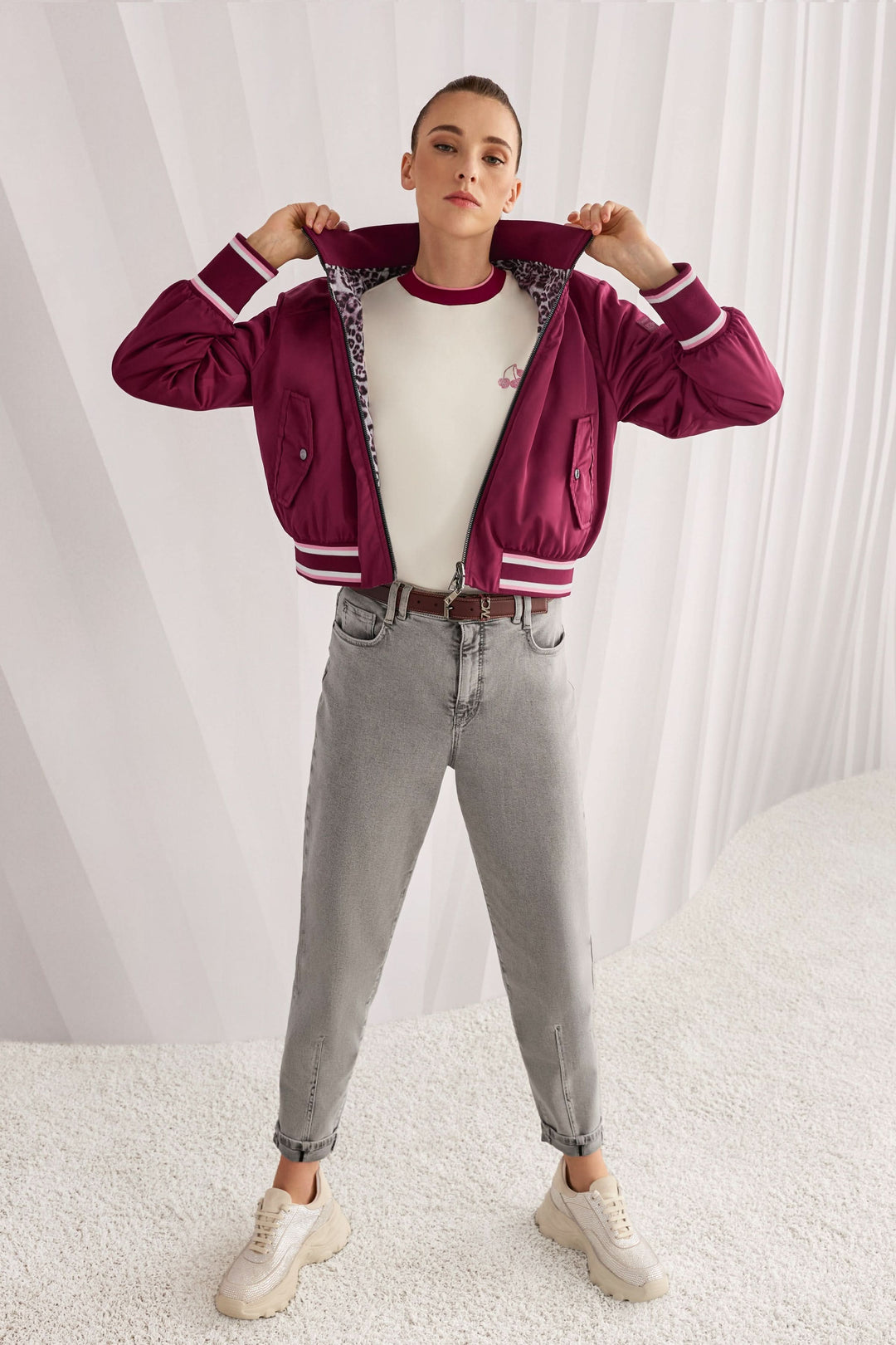 Femme portant un T-shirt classique avec col contrasté et logo Marc Cain Sport, associé à une veste rouge et un jean décontracté.