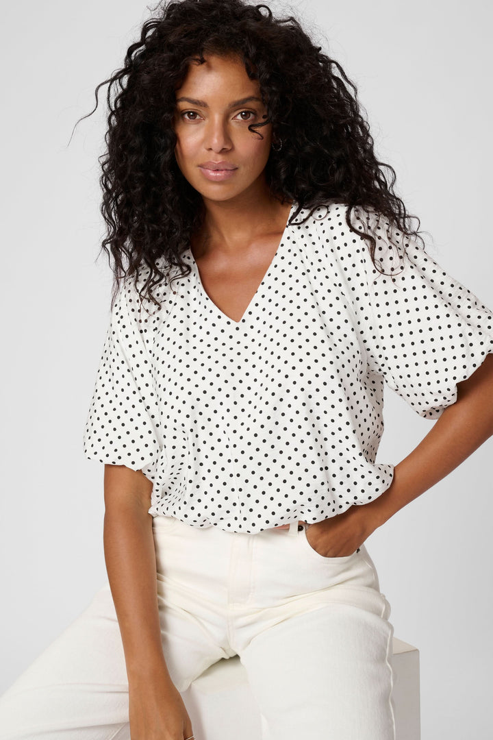 Blouse Gwen à pois, encolure en V, manches amples, style féminin moderne, portée avec un jean taille haute.