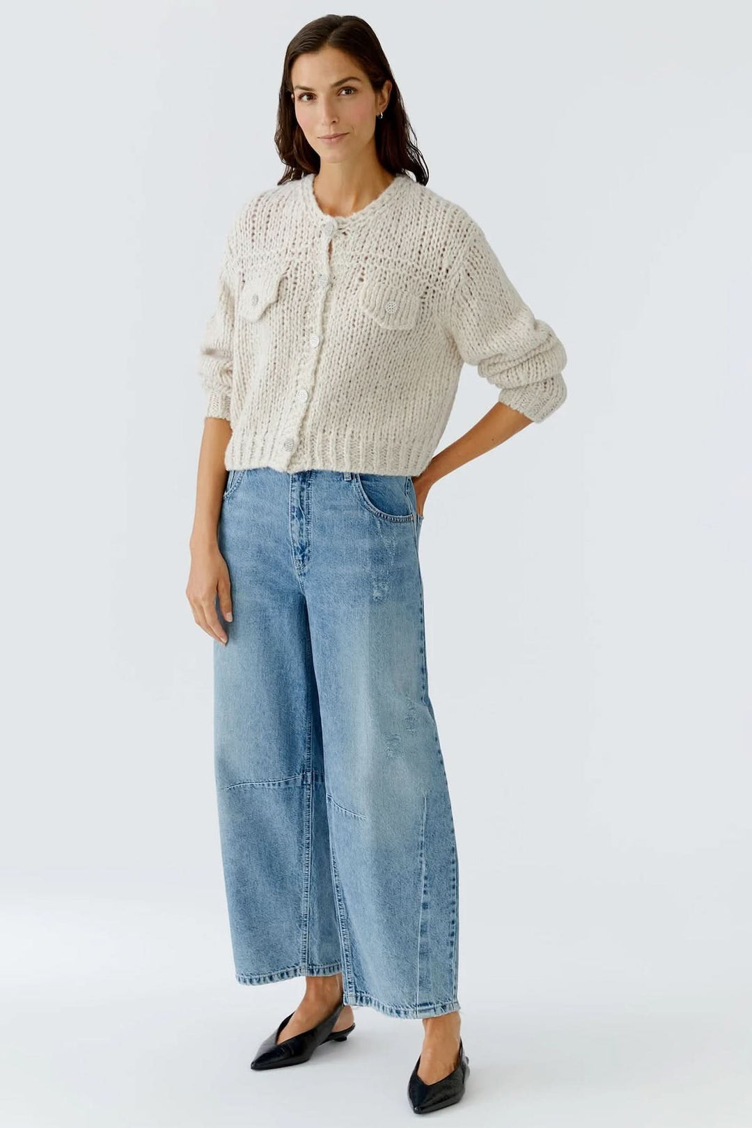 Femme portant une veste en tricot épais à boutons bijoux avec jean large, style automne-hiver chic et cosy.