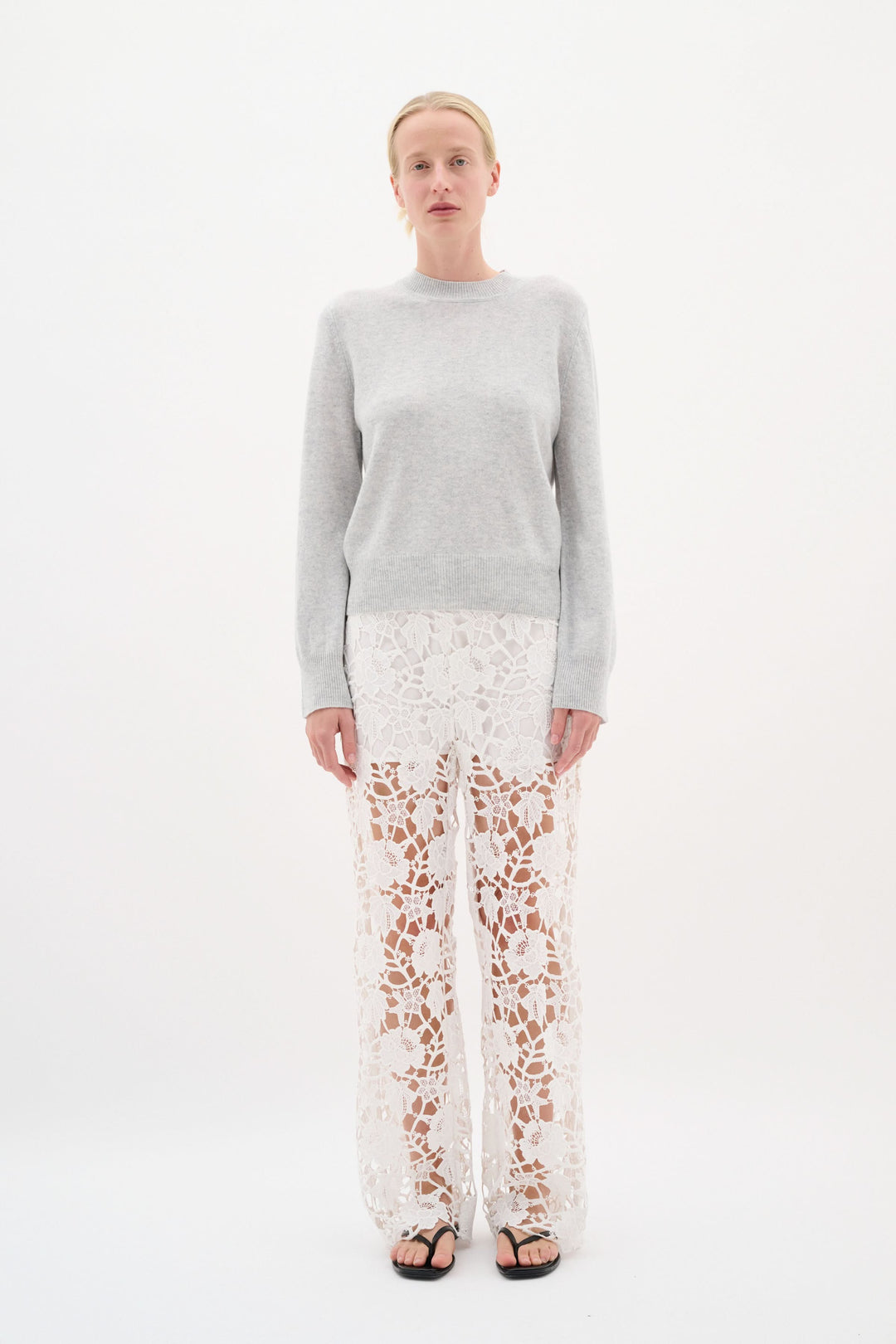 Modèle portant un chandail en maille douce avec un pantalon en dentelle blanche, créant un look élégant et raffiné.