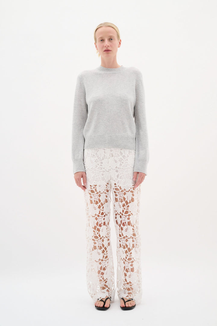 Modèle portant un chandail en maille douce avec un pantalon en dentelle blanche, créant un look élégant et raffiné.