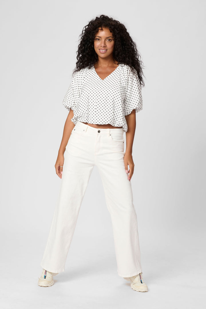 Femme portant un haut à pois Gwen à encolure en V avec manches amples, associé à un jean taille haute beige.