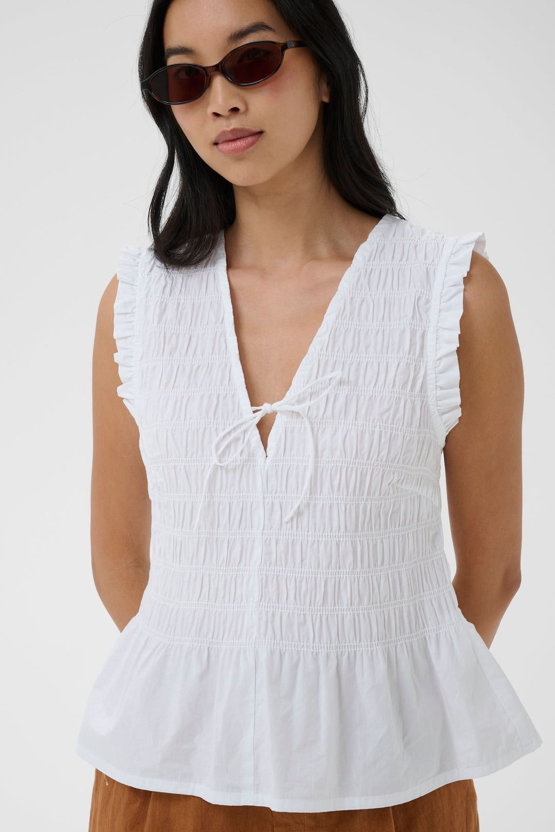 Femme portant une Blouse Borgny smockée sans manches à encolure nouée, idéale pour un style estival délicat et féminin.