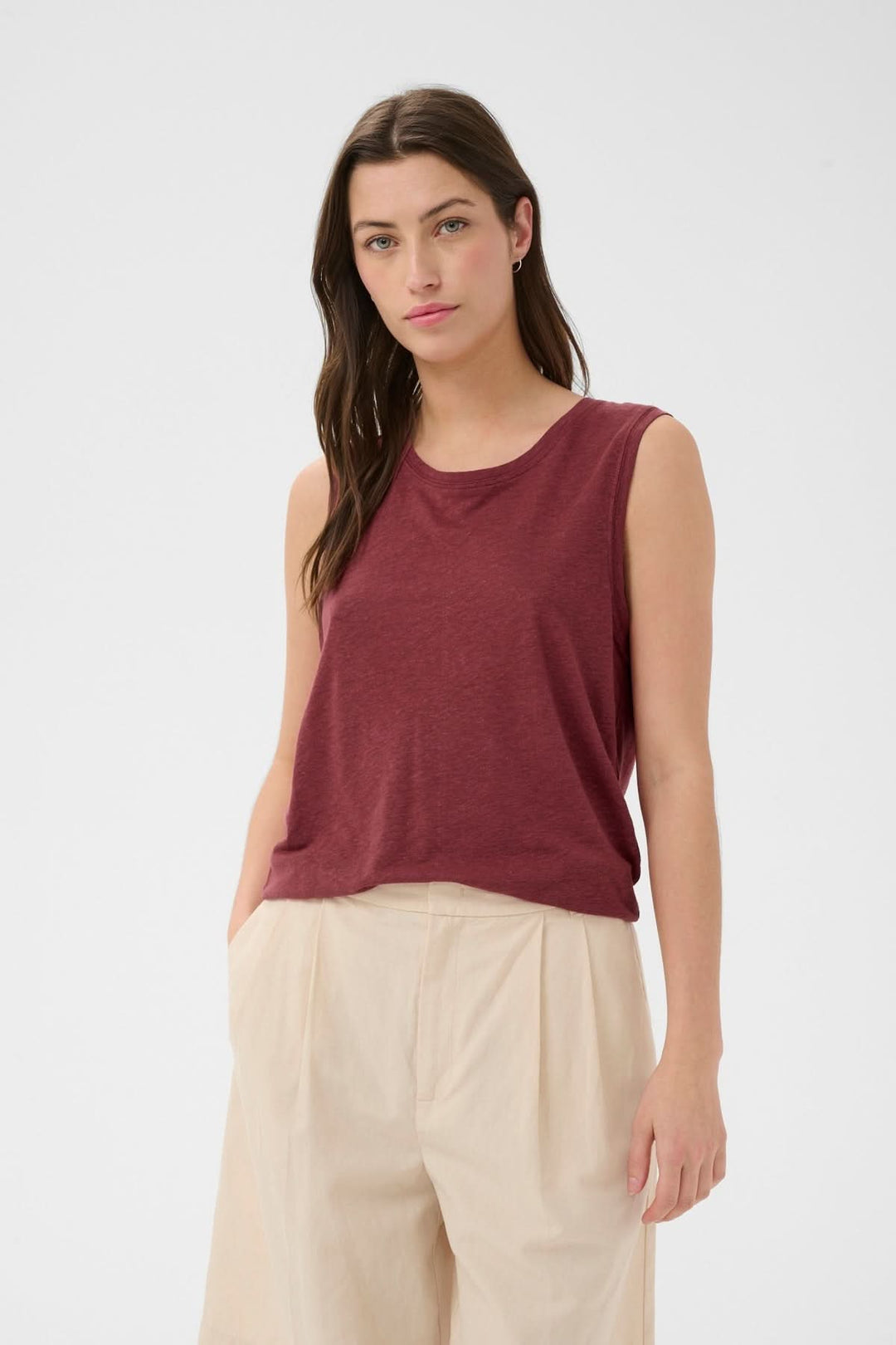 Femme portant la Cami fluide Buena bordeaux sans manches et coupe droite, combinée avec un pantalon beige pour un look polyvalent.