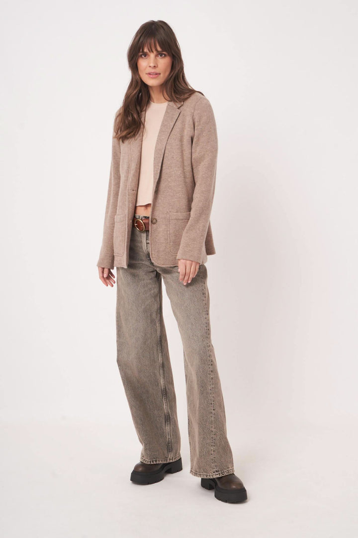 Femme portant un veston en maille beige avec une tenue décontractée en denim, alliant confort et style moderne.