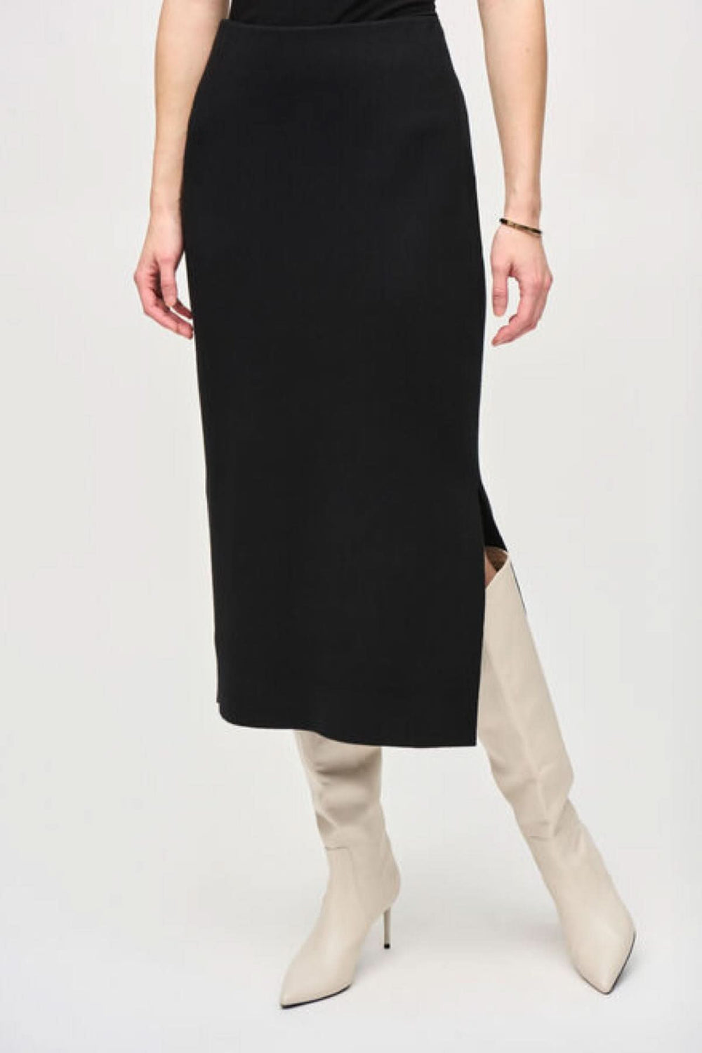 Jupe crayon en tricot noir avec fente, portée avec des bottes blanches, à la coupe midi élégante.