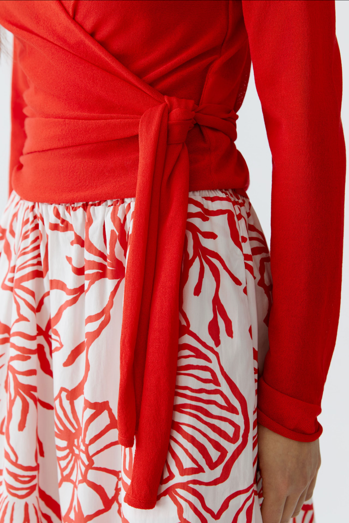 Chandail portefeuille rouge avec décolleté en V, associé à une jupe blanche à motifs floraux.
