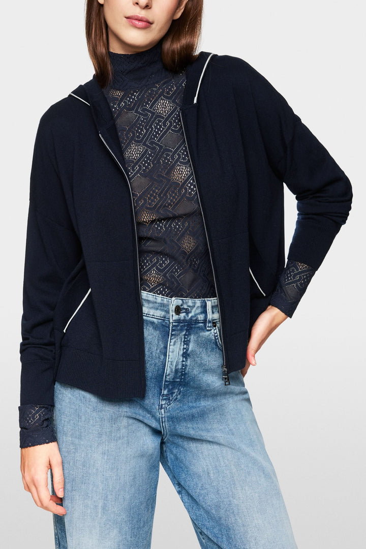 Cardigan tricoté à capuchon zippé, style décontracté avec détails contrastants, porté avec un top à motifs.