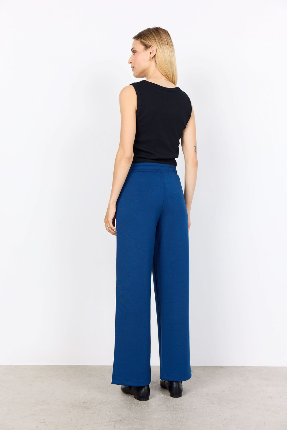 Femme portant un pantalon large bleu avec cordon à l'arrière, associé à un haut noir ajusté.