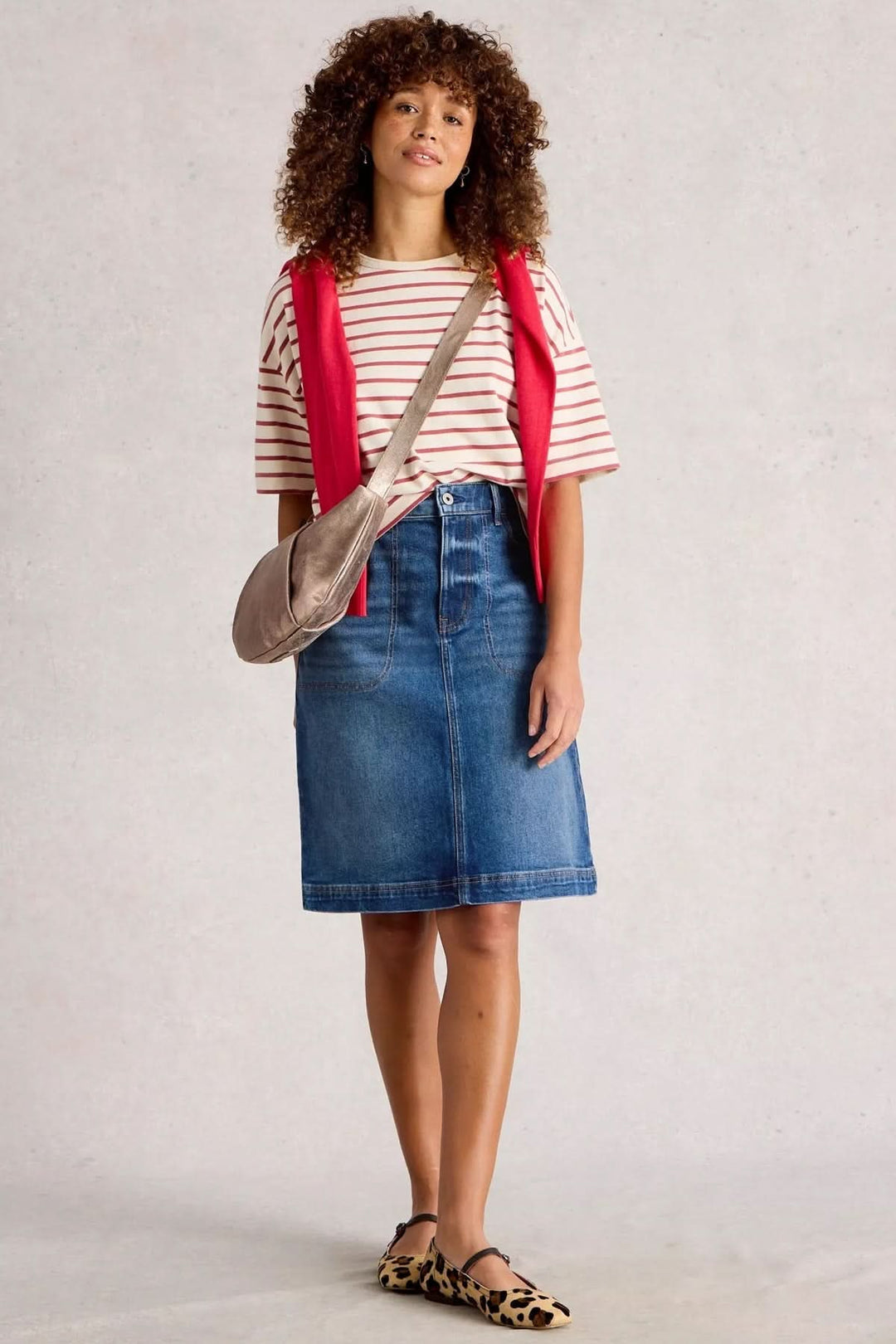 Femme portant une jupe en denim bleu, t-shirt rayé et gilet rouge pour un look casual chic.