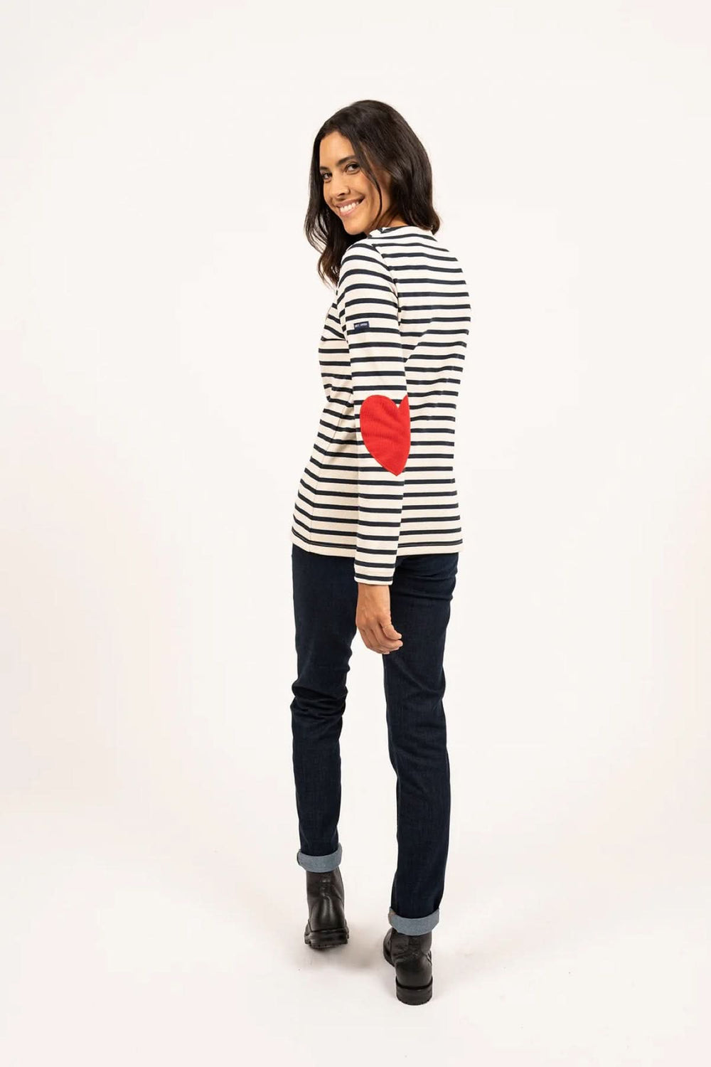 Femme portant un chandail marinière avec coudières en cœur, jean brut et bottines, look casual moderne.