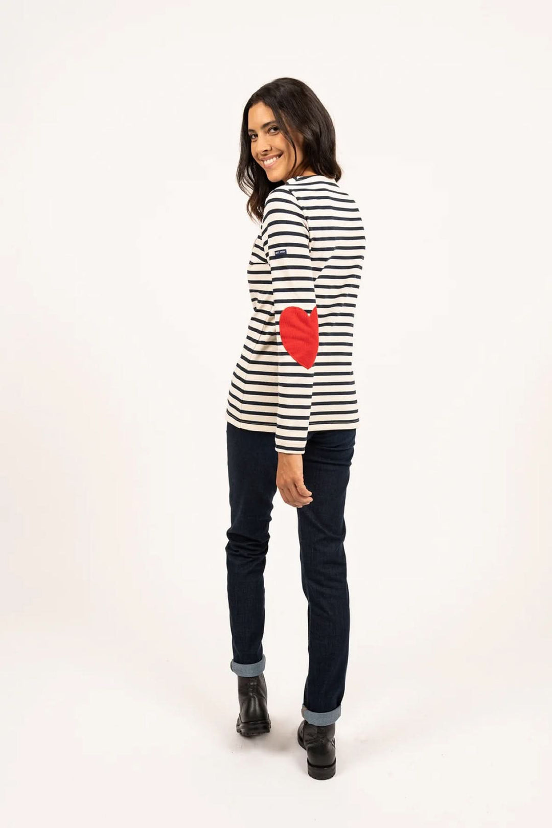 Femme portant un chandail marinière avec coudières en cœur, jean brut et bottines, look casual moderne.