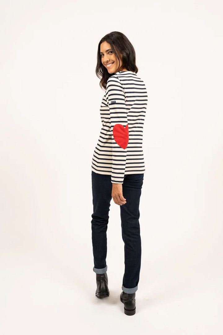 Femme portant un chandail marinière avec coudières en cœur, jean brut et bottines, look casual moderne.