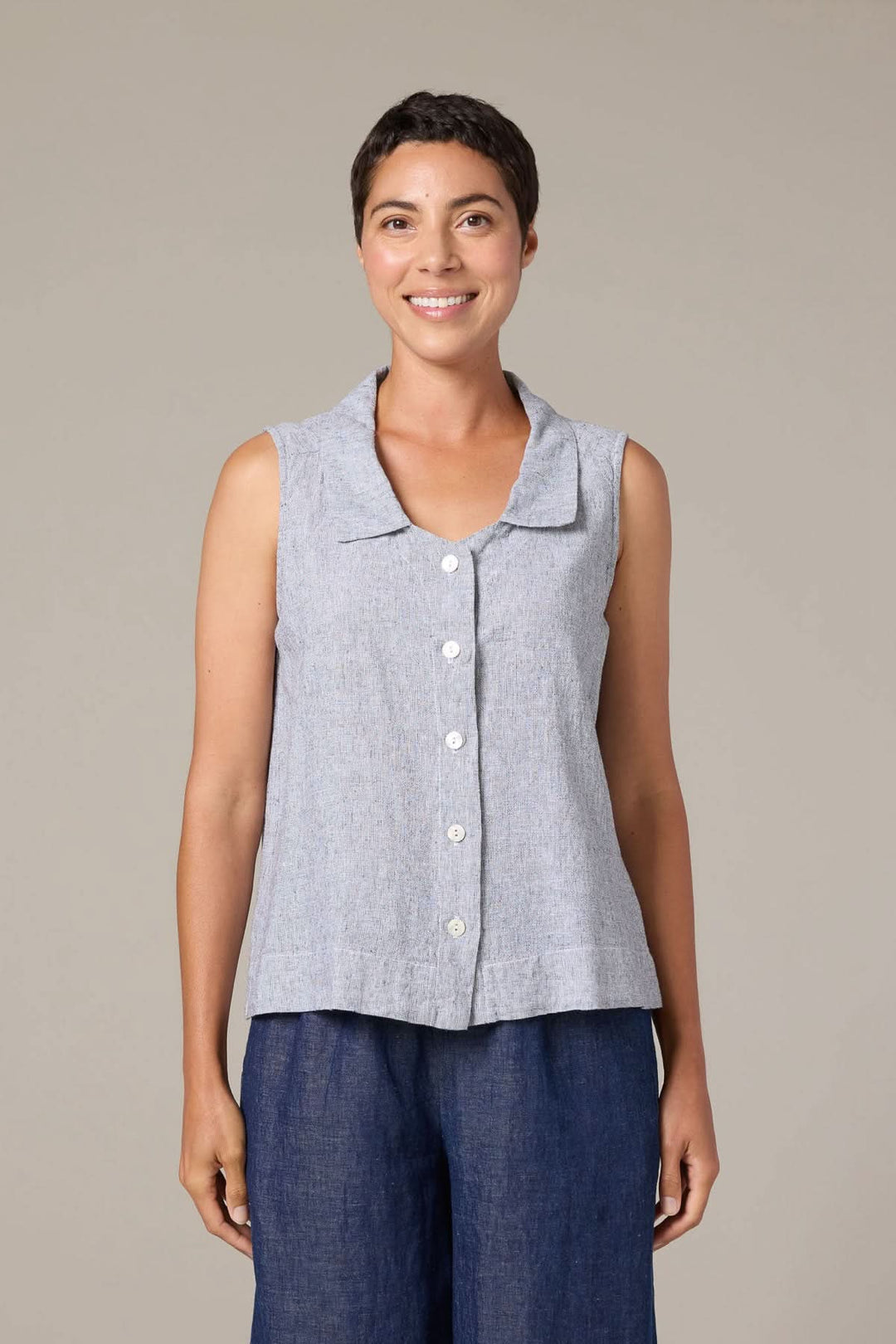 Femme portant une camisole col chemise boutonnée en lin gris sans manches avec pantalon bleu.