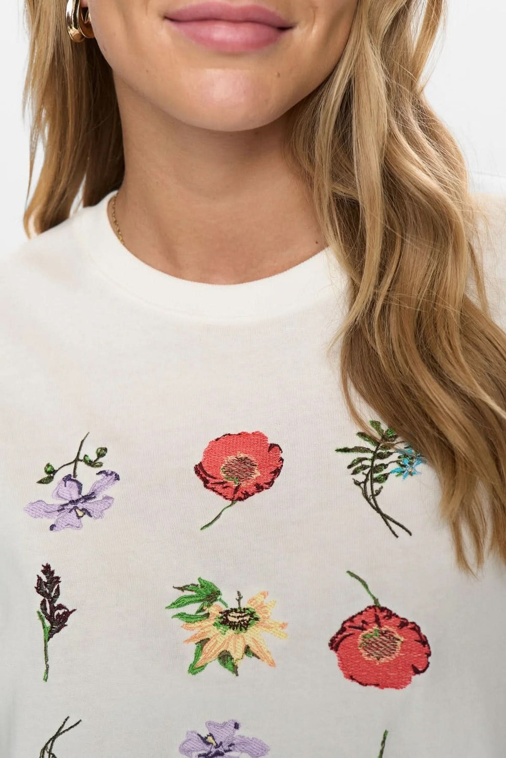 T-shirt à broderies florales avec motifs colorés sur fond blanc, style minimaliste et moderne, coupe ample pour un confort quotidien.