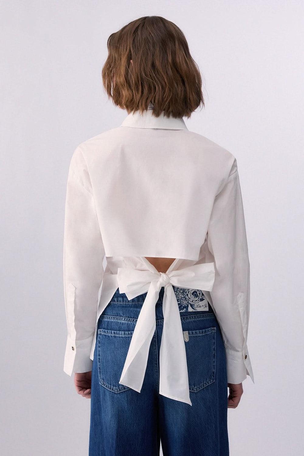 Femme portant une chemise à nouer au dos élégante, vue de dos, mettant en valeur le détail noué qui offre une touche moderne et féminine.
