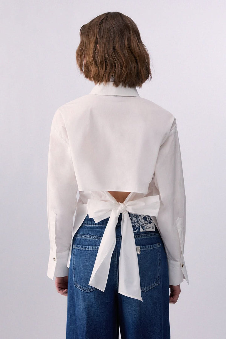 Femme portant une chemise à nouer au dos élégante, vue de dos, mettant en valeur le détail noué qui offre une touche moderne et féminine.