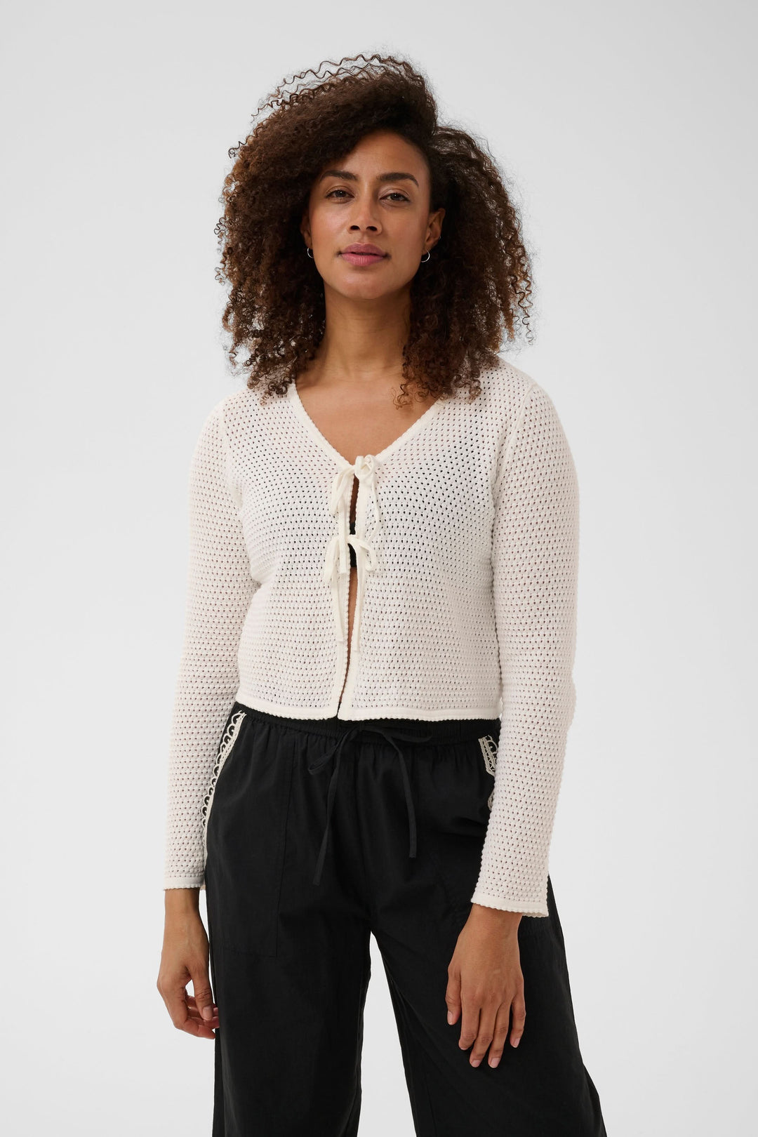 Femme portant le Cardigan Rosefina en maille ajourée à nouer, élégant et léger, avec encolure en V et manches longues.