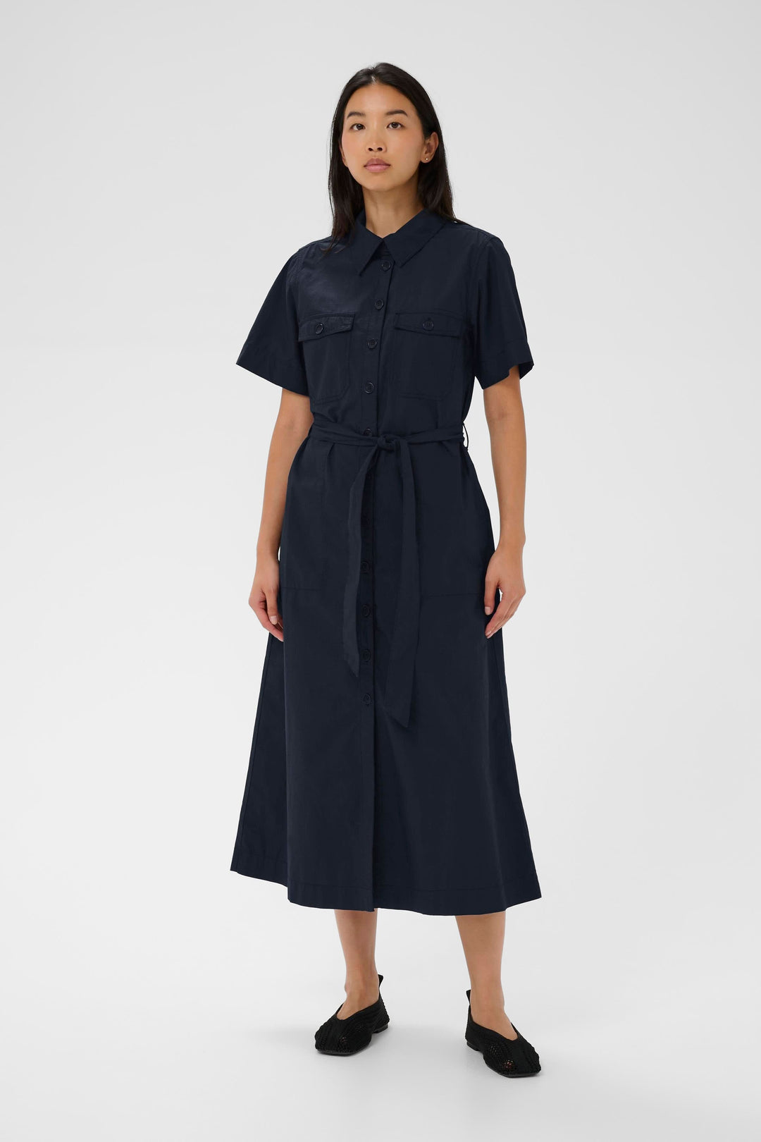 Femme portant la Robe Ariel chemise longue ceinturée manches courtes avec poches poitrine et ceinture, coupe élégante et moderne.