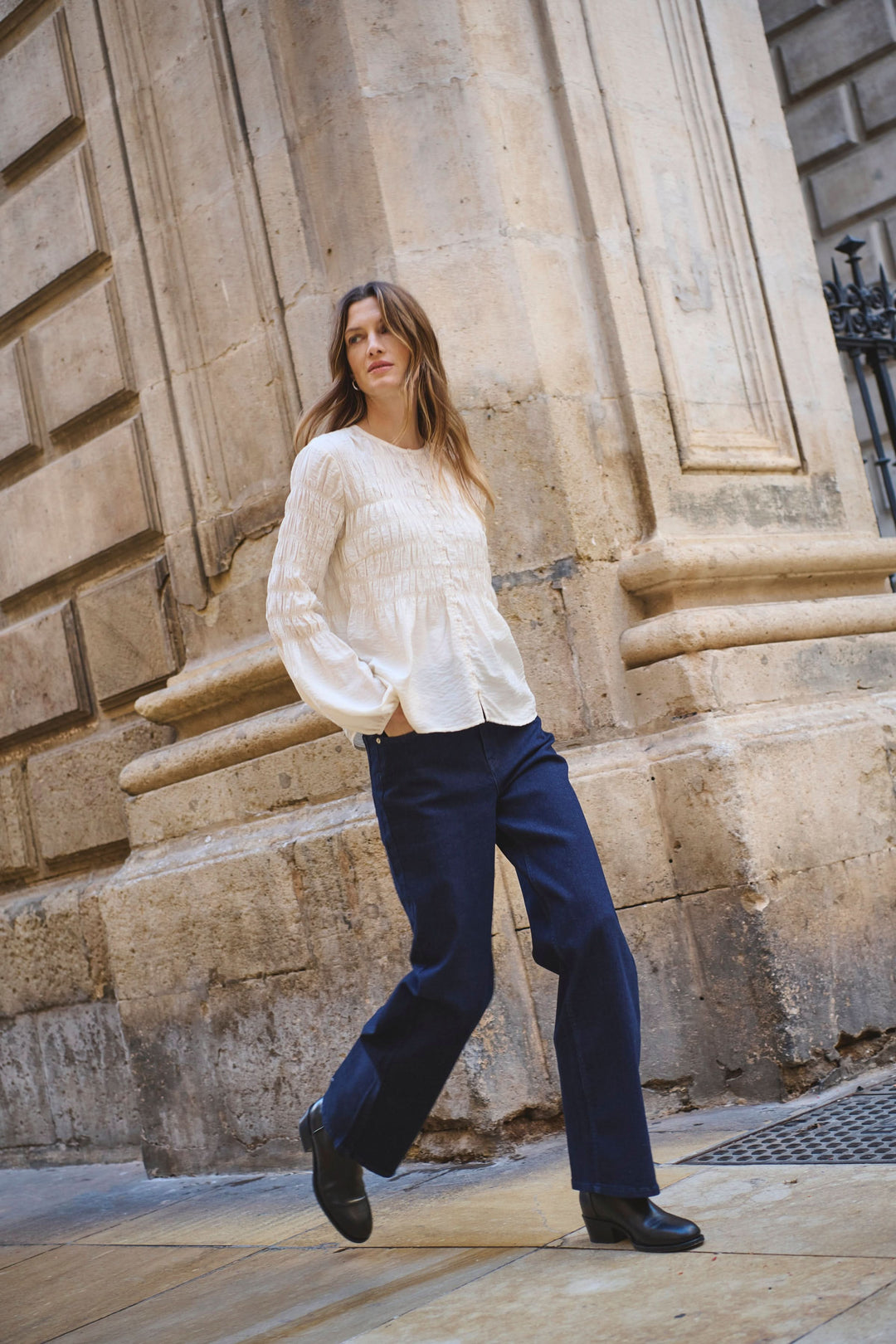 Femme marchant dans une rue avec un jean Simona à jambe droite et un haut blanc, backdrop élégant.