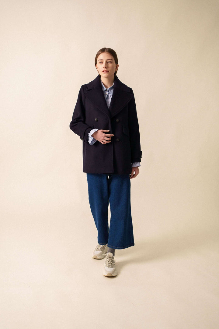 Manteau chic bleu marine avec encolure en V, présenté par une femme dans une tenue décontractée.