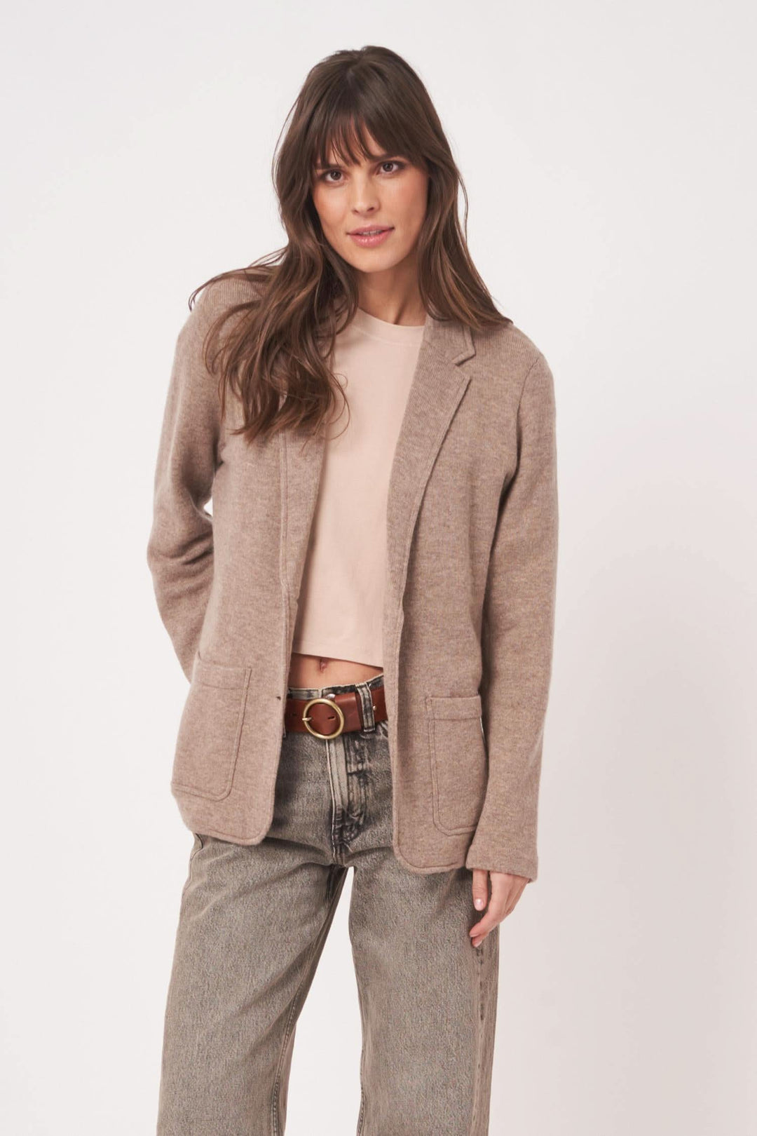 Femme portant un veston en maille beige, avec un look décontracté et moderne, idéal pour des superpositions élégantes.