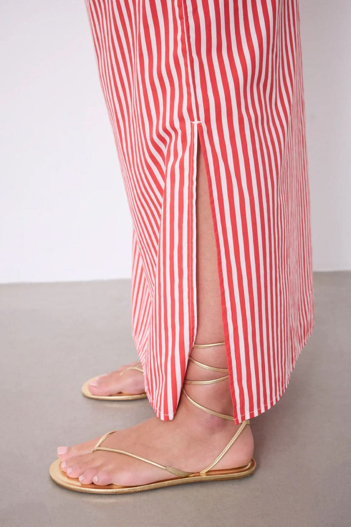 Jupe Ilona longue rayée taille élastique avec motif rayé vertical, fente latérale et sandales dorées, offrant une silhouette fluide.