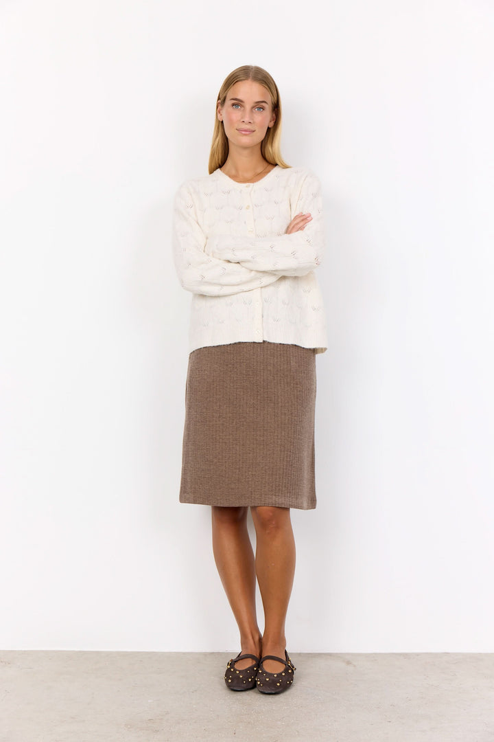 Femme portant un cardigan ajouré blanc avec boutons et une jupe midi texturée marron.