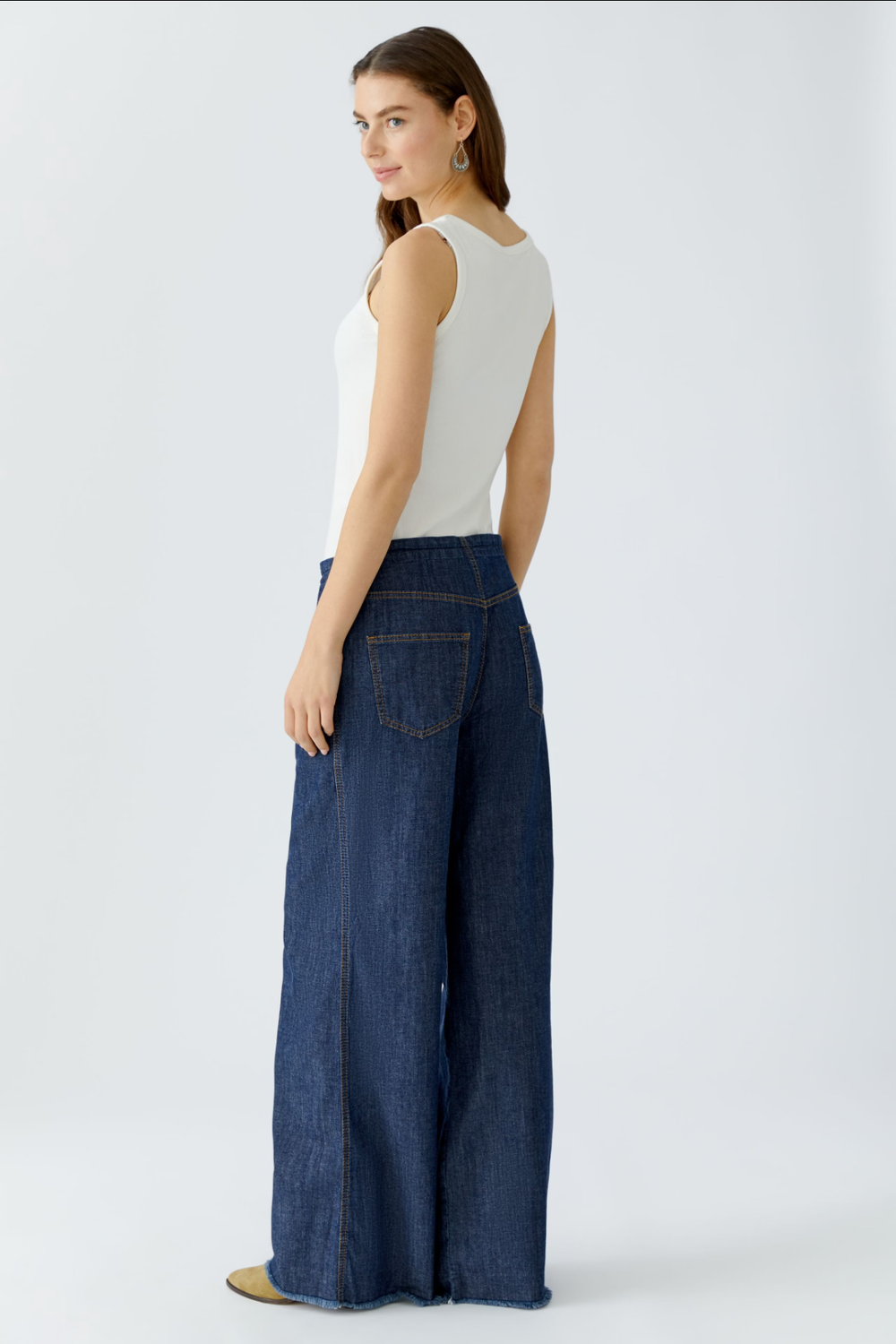 Femme portant un jean ultra léger à coupe large, vue arrière, avec un haut blanc, montrant style moderne et fluide.