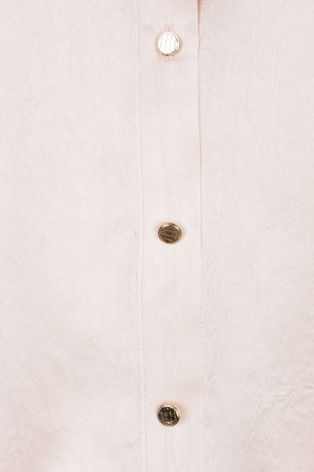 Détails d'une blouse satinée avec boutons brillants sur fond doux, parfaite pour un look élégant.