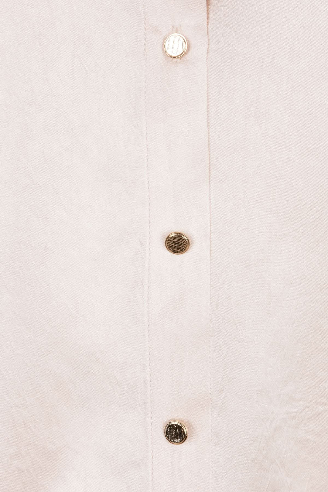 Détails d'une blouse satinée avec boutons brillants sur fond doux, parfaite pour un look élégant.