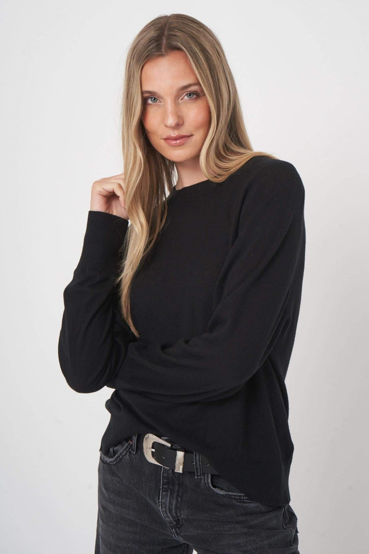 Chandail en laine noir avec coupe droite et finitions côtelées, porté par une femme souriante.