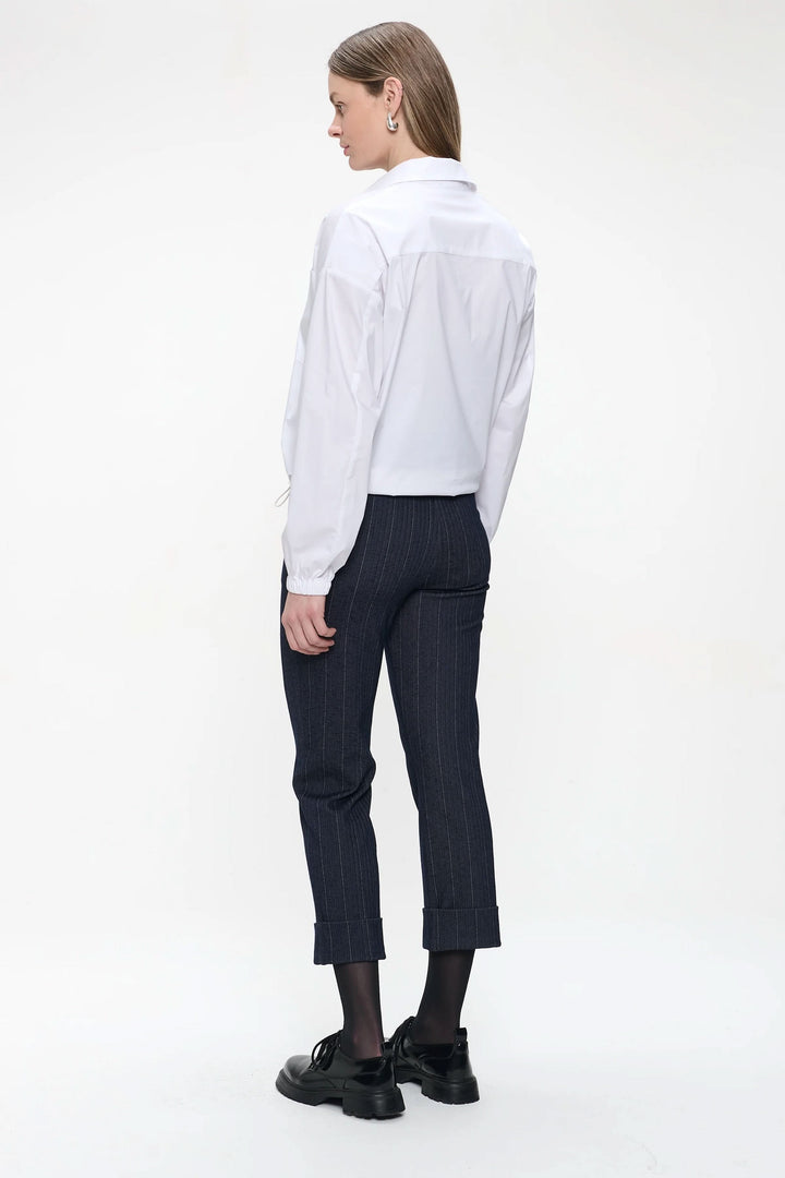 Femme de dos portant un pantalon à pinces noir à rayures avec une chemise blanche, look moderne et élégant.