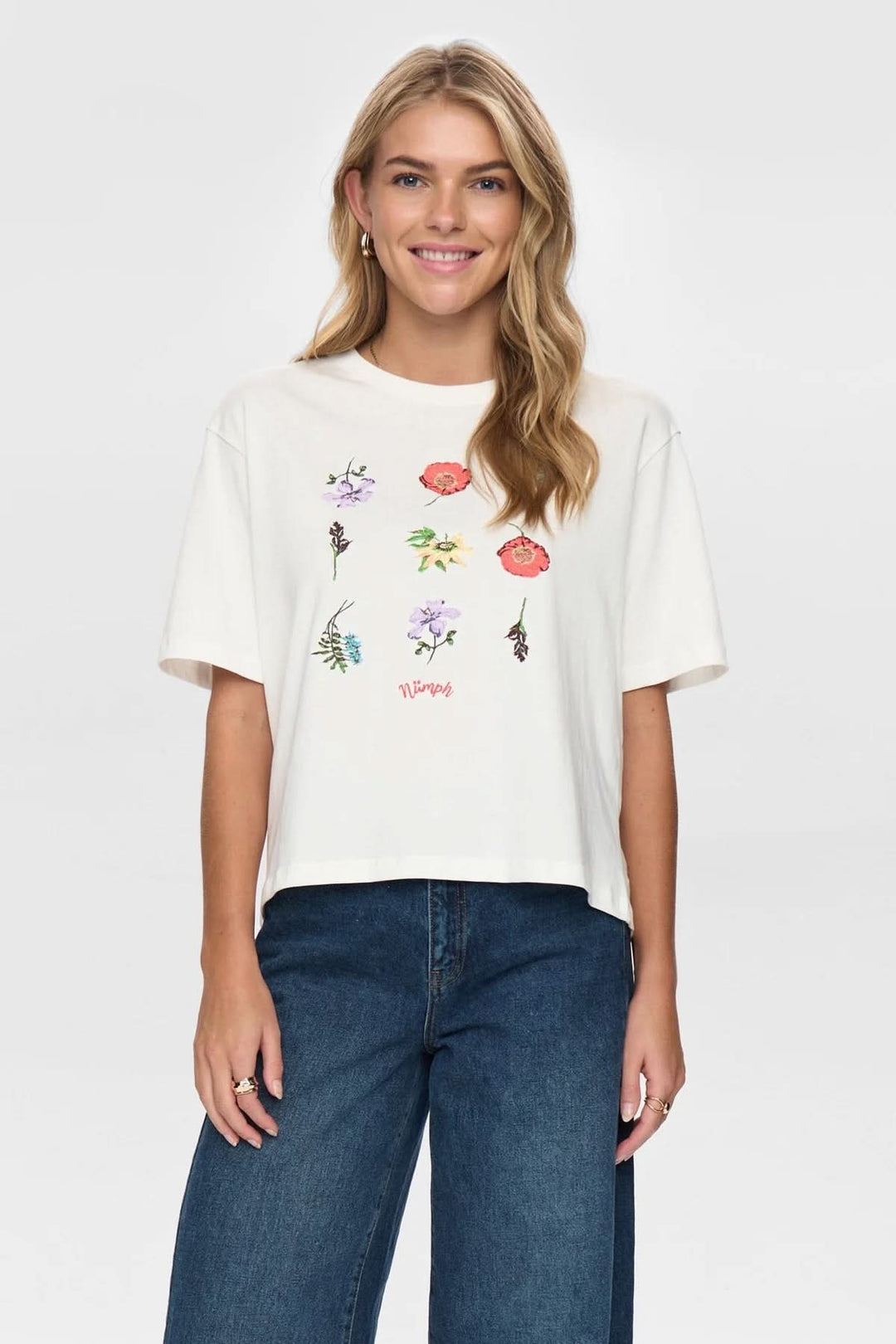 Modèle portant un T-shirt à broderies florales avec col rond et manches courtes, offrant un style moderne et féminin.