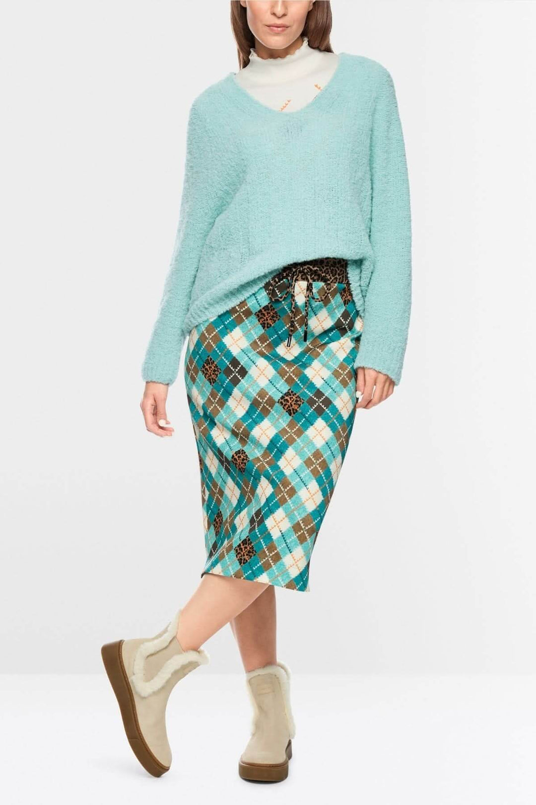 Femme portant un chandail tricoté bleu à col en V avec jupe à carreaux, look hivernal et moderne cosy.