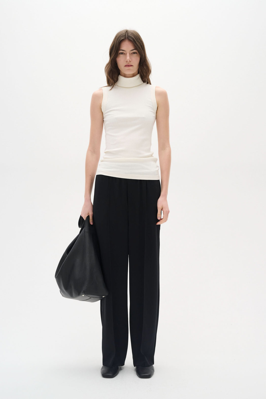 Femme en camisole Dagna col montant et pantalon noir, tenant un sac, style élégant et confortable.