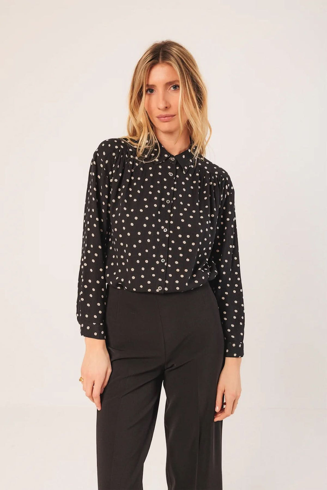 Femme portant une chemise noire imprimée et un pantalon droit à coupe fluide noir, style décontracté et élégant.