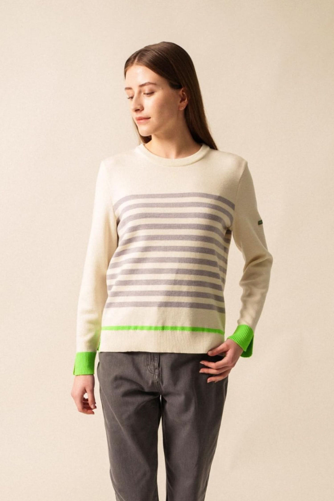 Chandail Evian à rayures grises et blanches avec finitions fluo vertes, porté avec un pantalon gris.