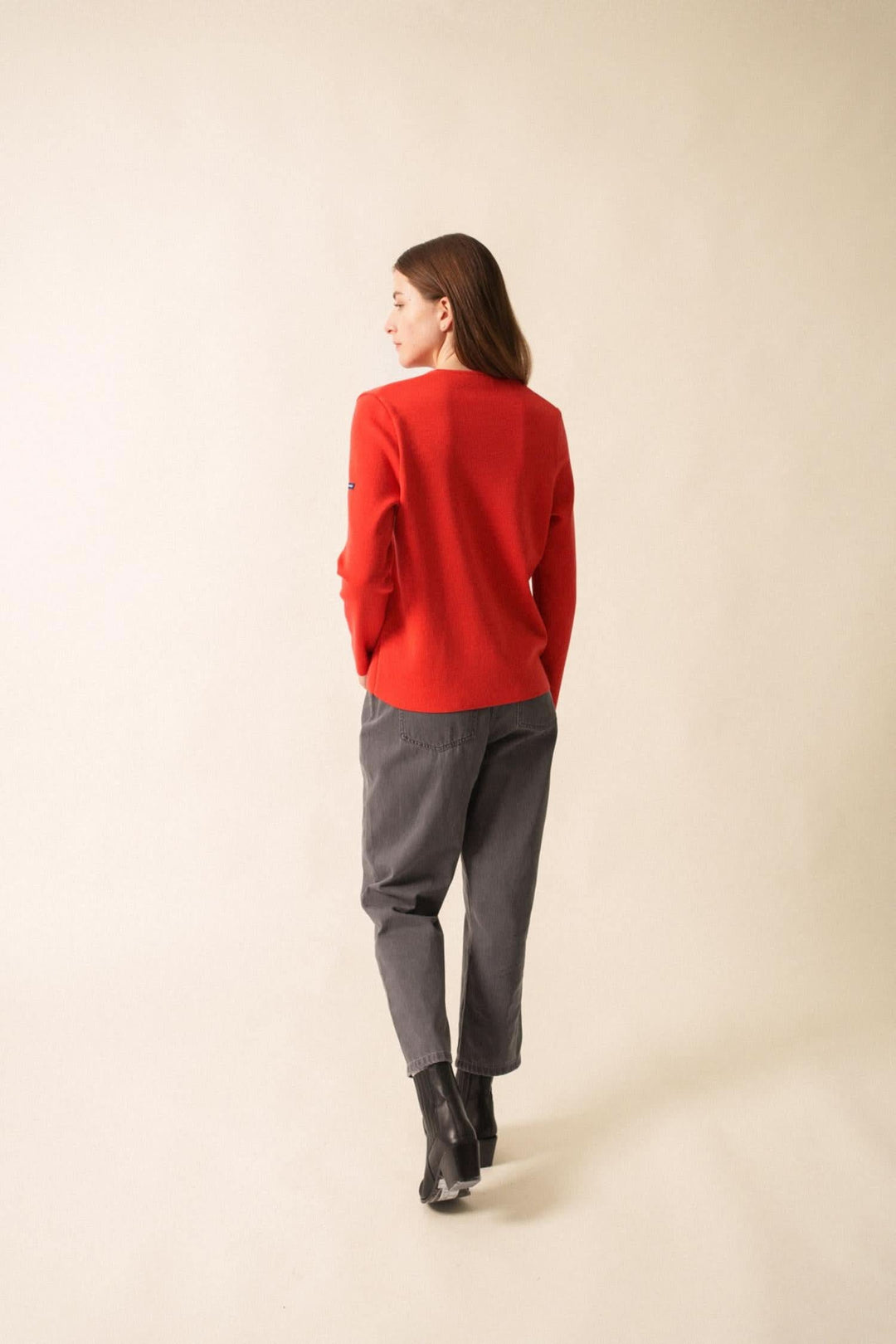 Femme vue de dos portant un gilet rouge avec pantalon gris, style casual chic sur fond neutre.