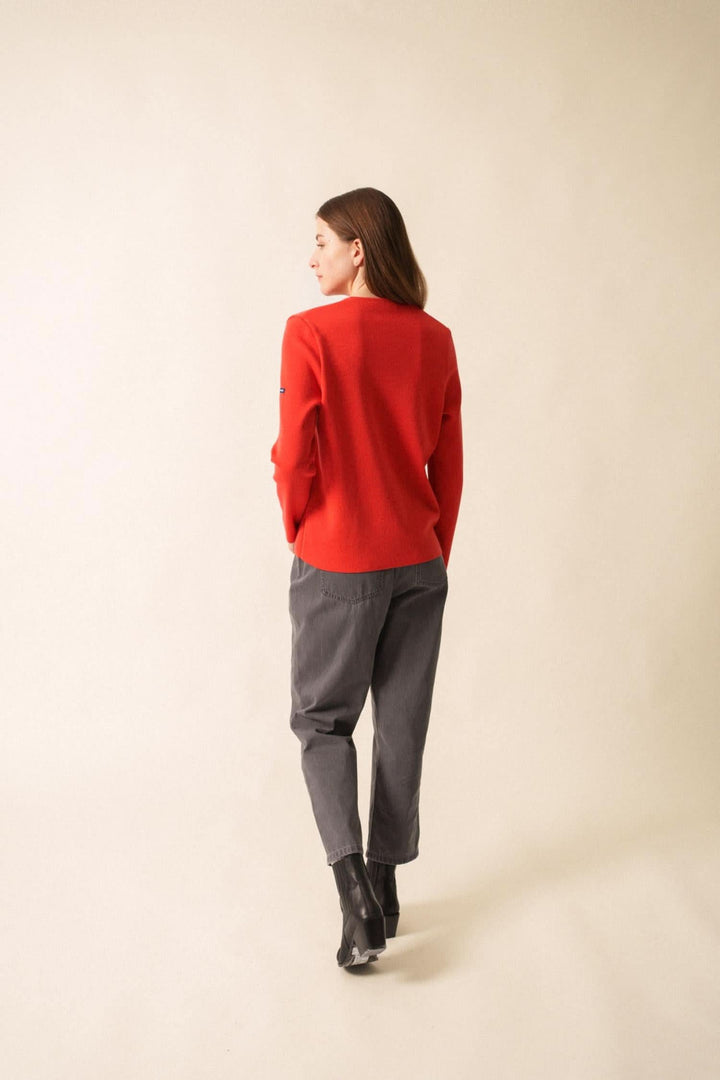 Femme vue de dos portant un gilet rouge avec pantalon gris, style casual chic sur fond neutre.