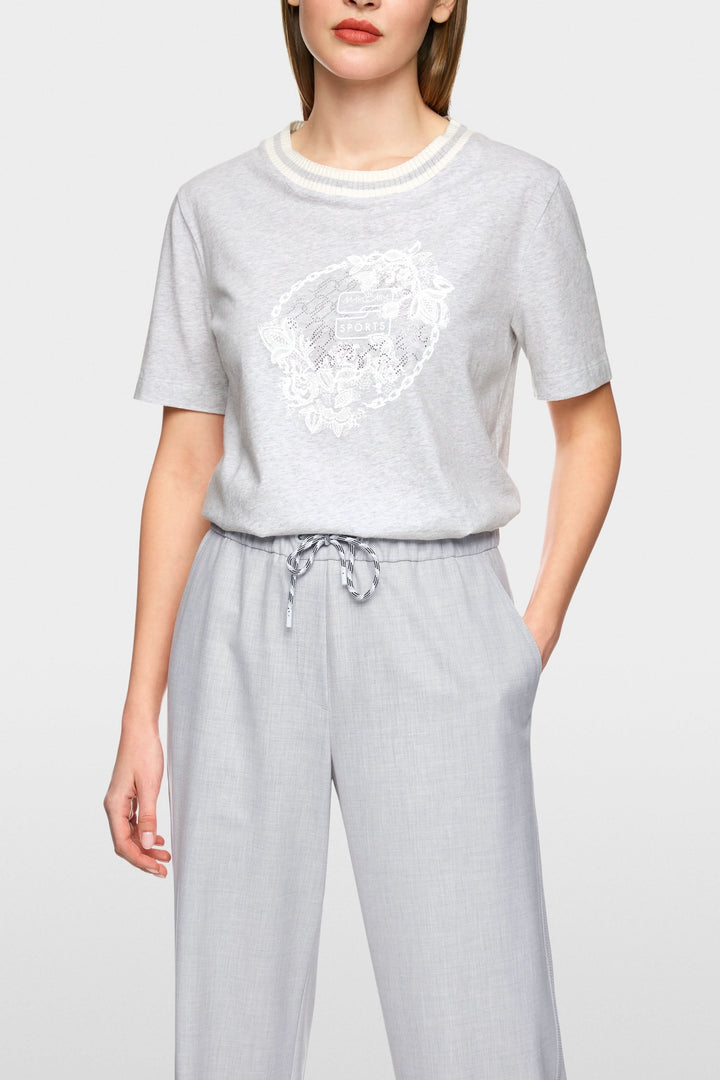 T-shirt gris avec broderie florale ton sur ton et encolure côtelée, porté avec un pantalon léger.