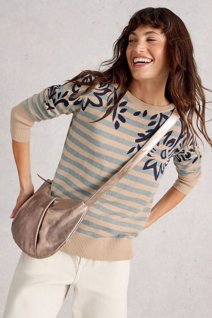Femme souriante portant un chandail à rayures avec motif floral, un sac bandoulière, et un style décontracté.