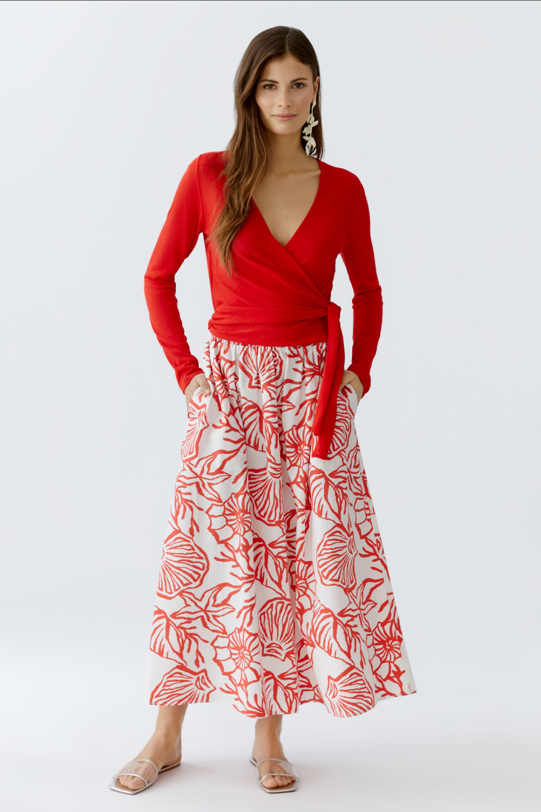 Chandail portefeuille rouge avec décolleté en V, associé à une jupe longue à motifs floraux.