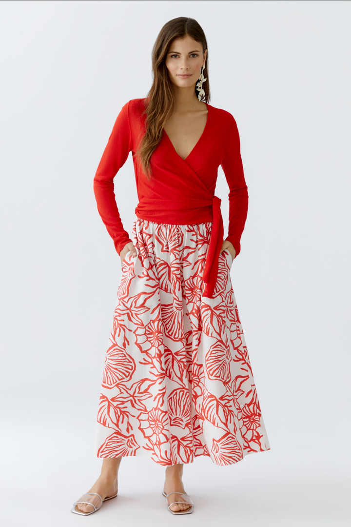 Chandail portefeuille rouge avec décolleté en V, associé à une jupe longue à motifs floraux.