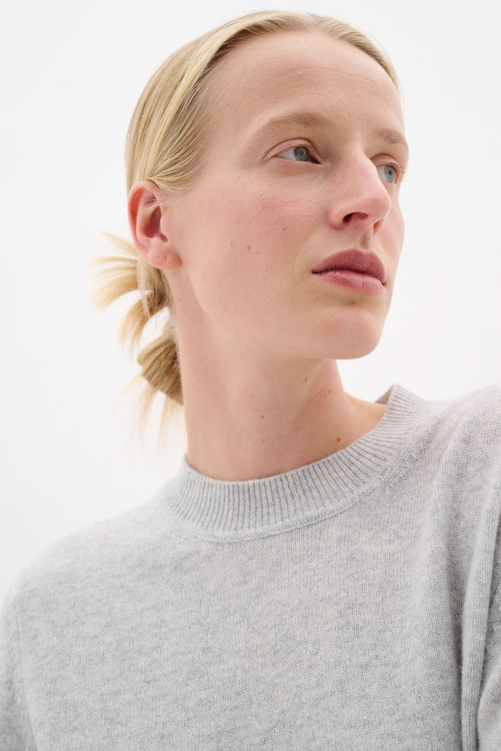 Modèle portant un chandail Silje en maille fine, couleur gris clair, avec encolure ronde et coupe droite.