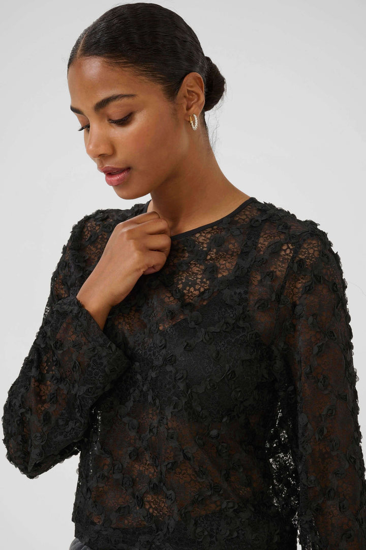 Blouse Rosie en dentelle florale à manches longues portée par une femme, manches longues évasées, dentelle transparente noire.