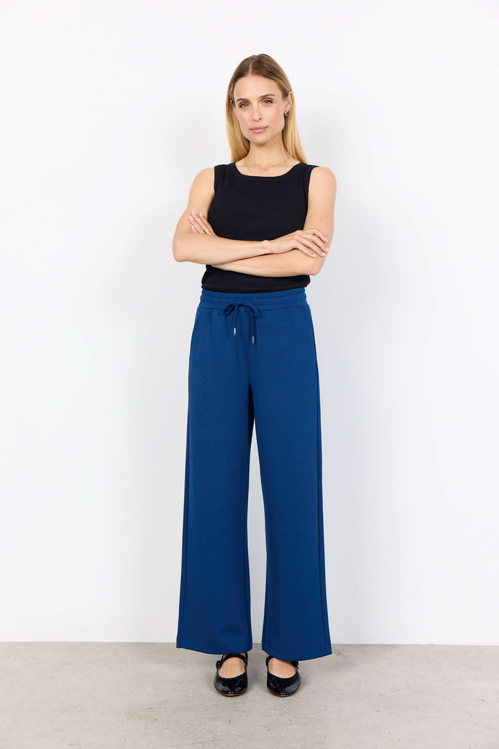 Pantalon avec cordon, jambe large fluide en tissu extensible, porté avec un top noir.