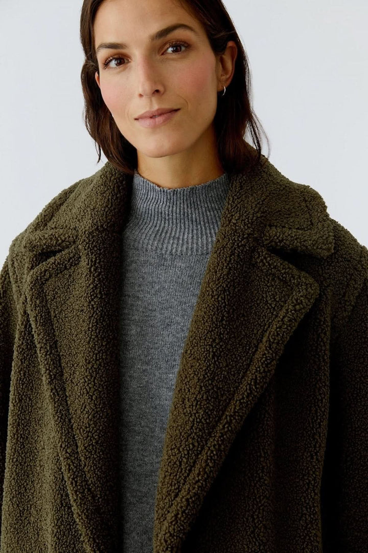 Femme portant un manteau long en tissu bouclette vert olive, chic et confortable pour les journées froides.