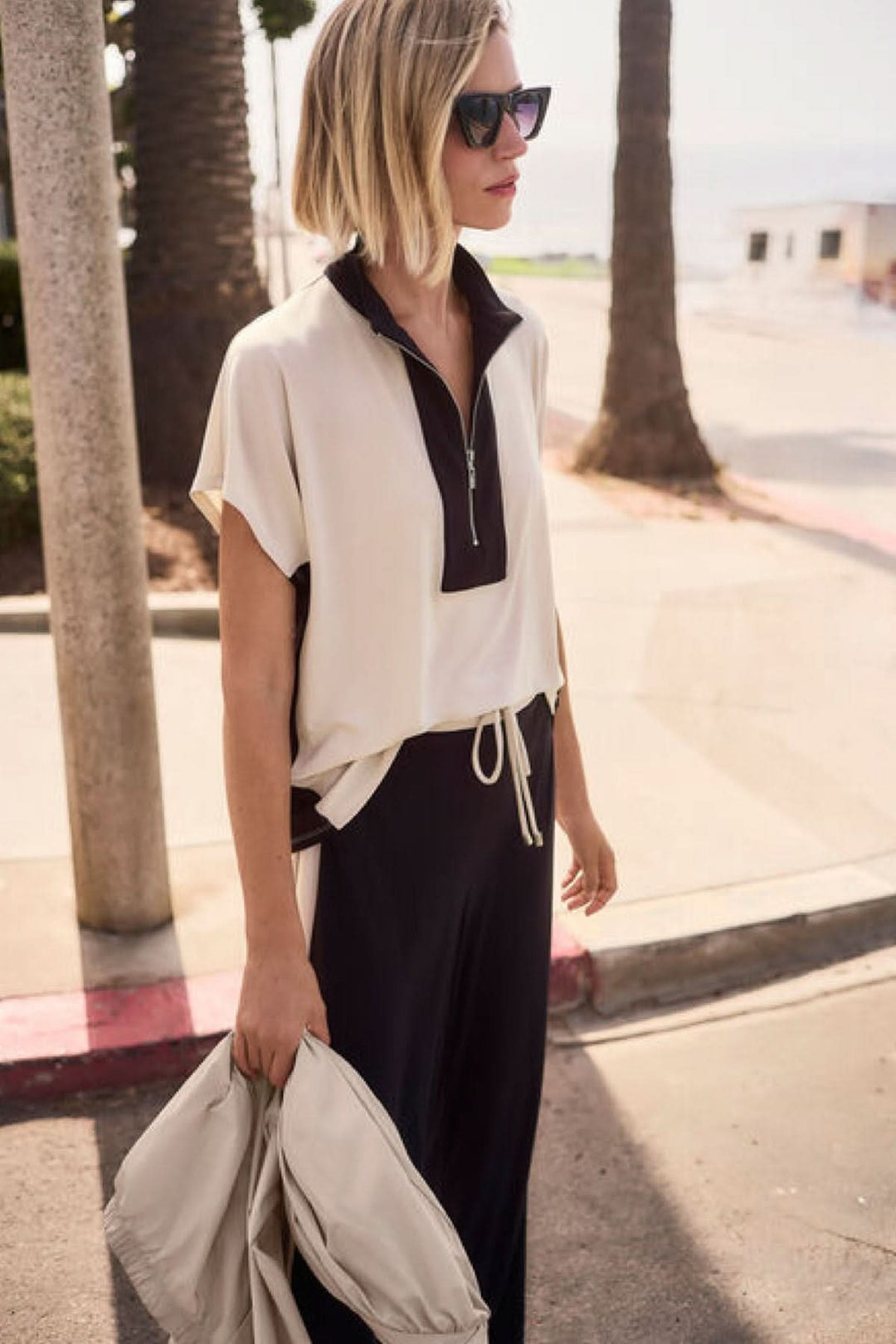 Femme portant un haut à col zippé structuré avec col montant, silhouette moderne et épurée, style sportif et raffiné.