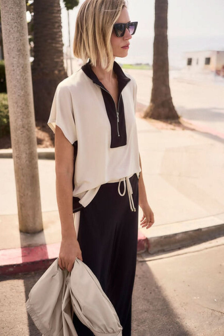 Femme portant un haut à col zippé structuré avec col montant, silhouette moderne et épurée, style sportif et raffiné.